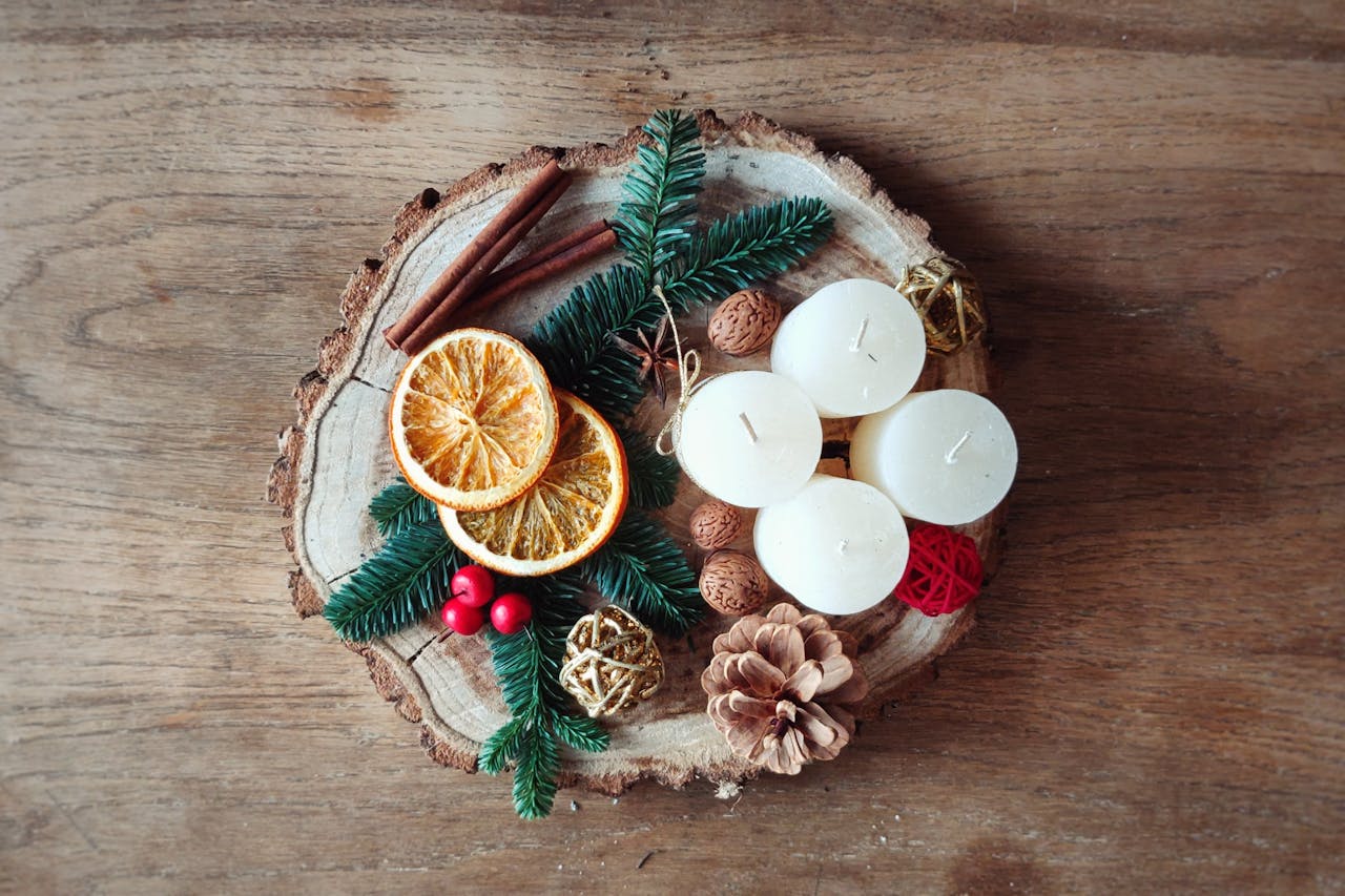 Decorative rustic arrangement with candles, dried oranges, and cinnamon on wood slab.